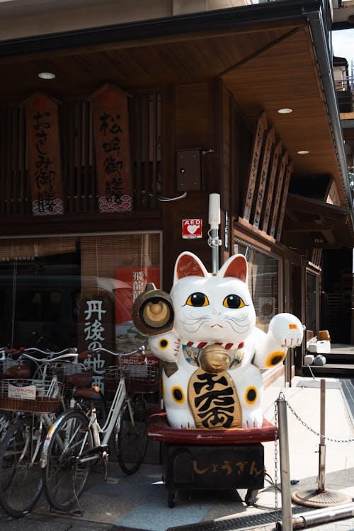 Free Lucky Maneki-neko Figurine Near the City Bike Stand Next to the Restaurant Stock Photo