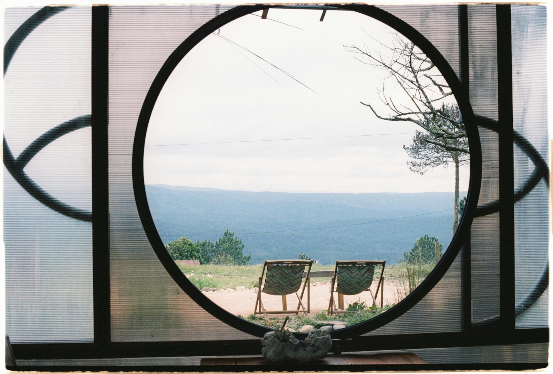 Tranquil landscape view through a circular window with sun loungers facing the mountains.