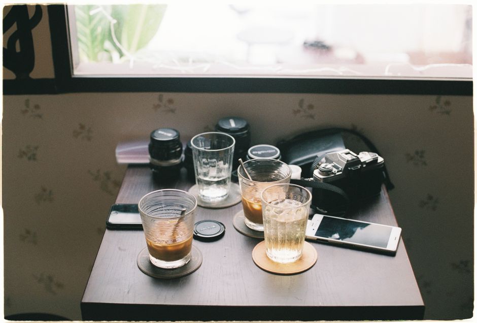 A café table with drinks, camera gear, and a smartphone in natural light.