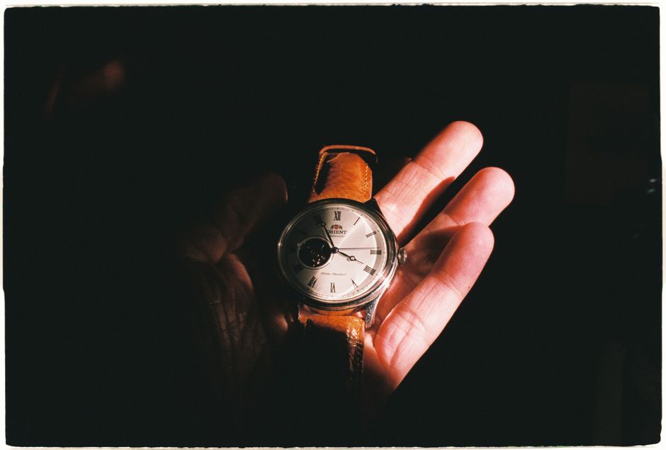 Close-up of a wristwatch with leather strap held in a hand, accented by dramatic lighting.