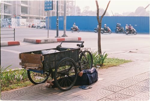 Free A man resting beside his cart on a city sidewalk, capturing the essence of urban life. Stock Photo