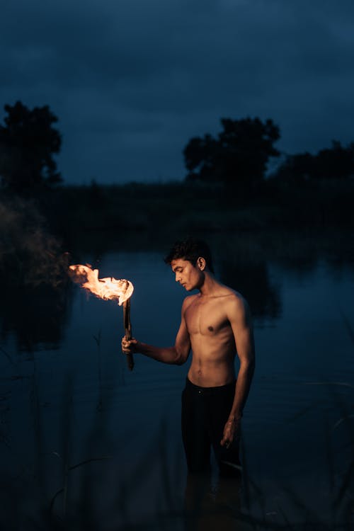 Topless Man Standing in Water and Holding Torch 