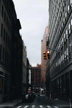 Moody view of a New York City street with tall buildings and traffic lights.