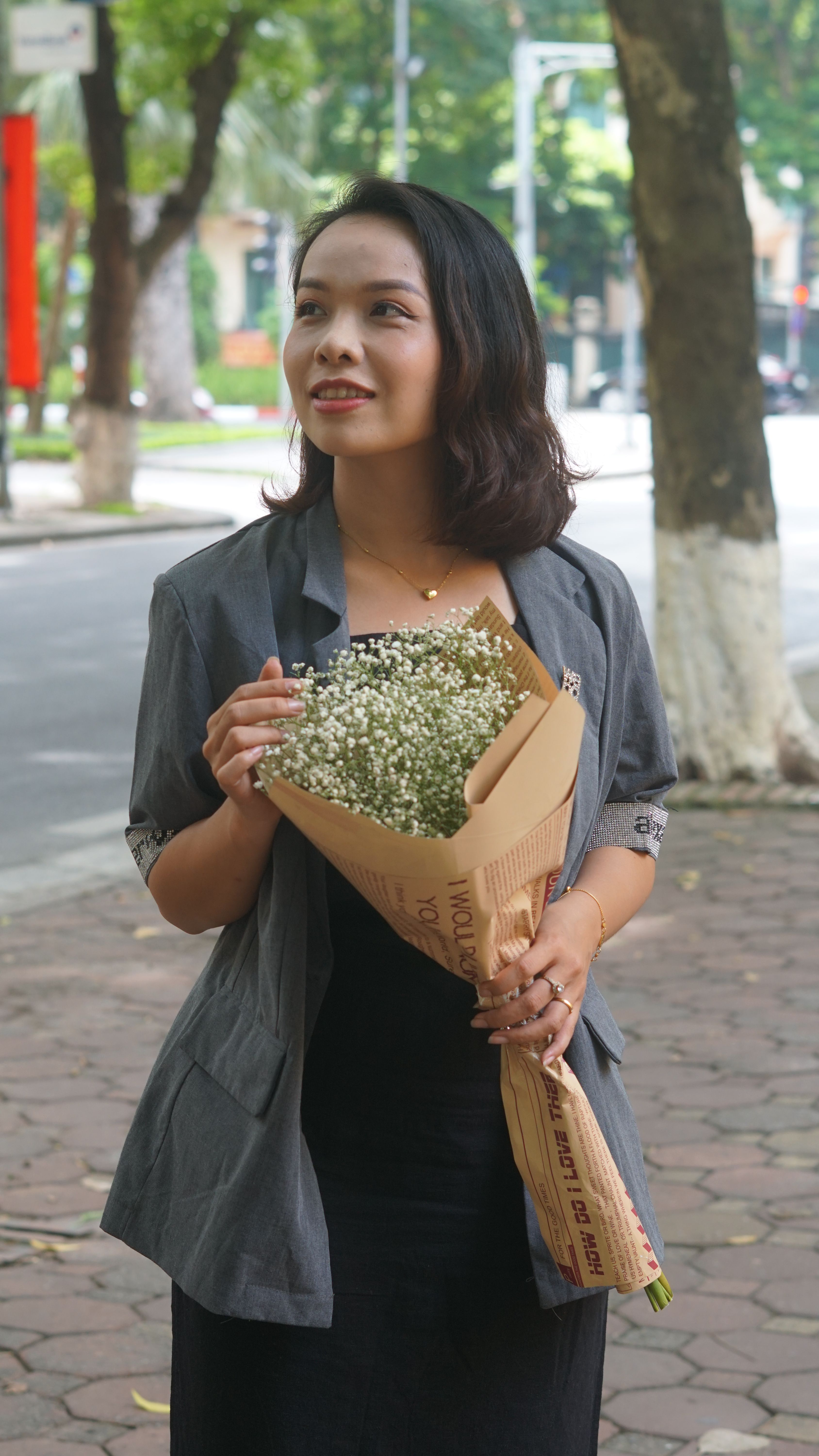 Woman smiling holding a flower bouquet outdoors in a park setting, showcasing an elegant and natural portrait.