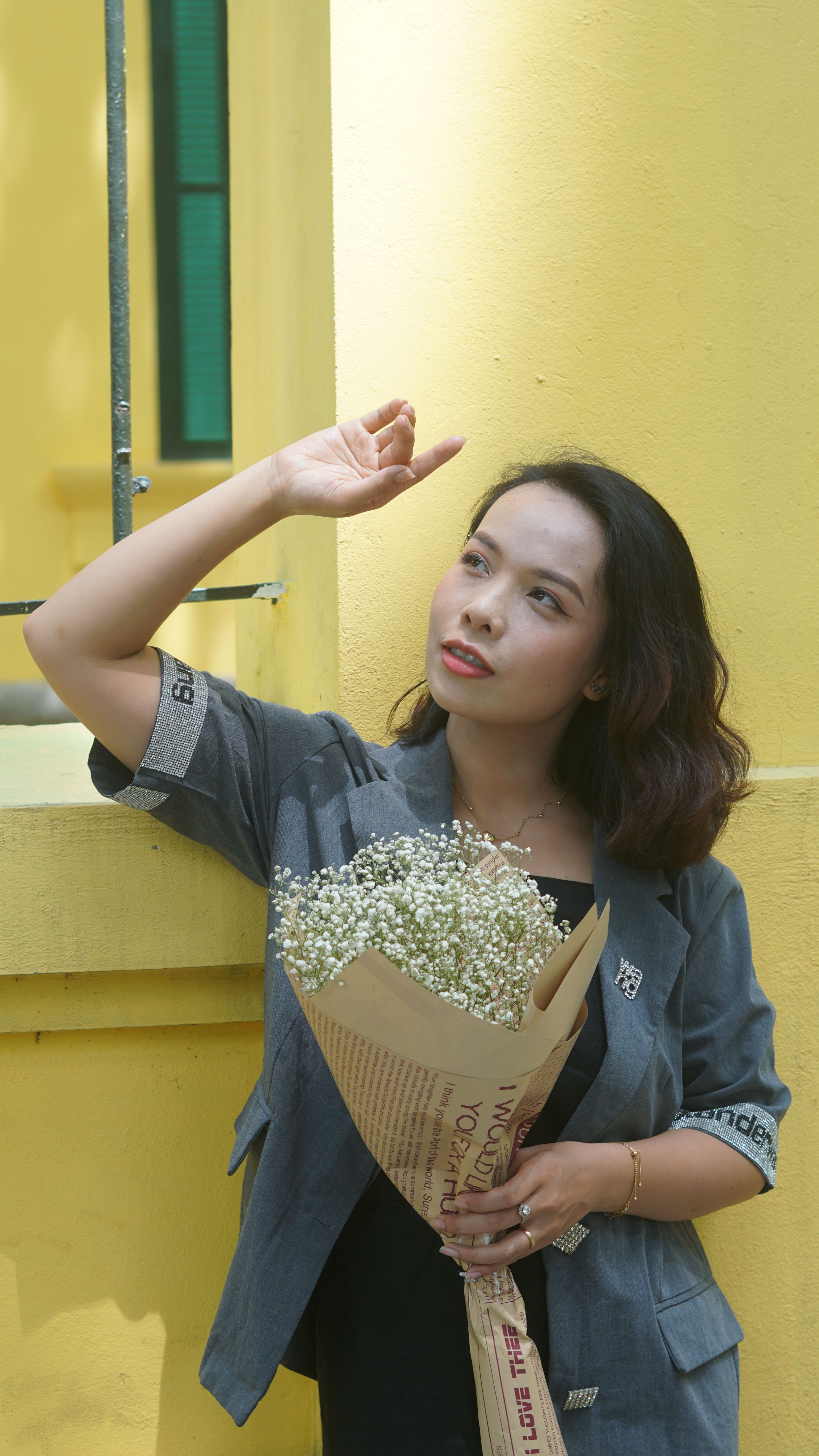 Woman admires the sky while holding a Baby's Breath bouquet against a vibrant yellow wall.