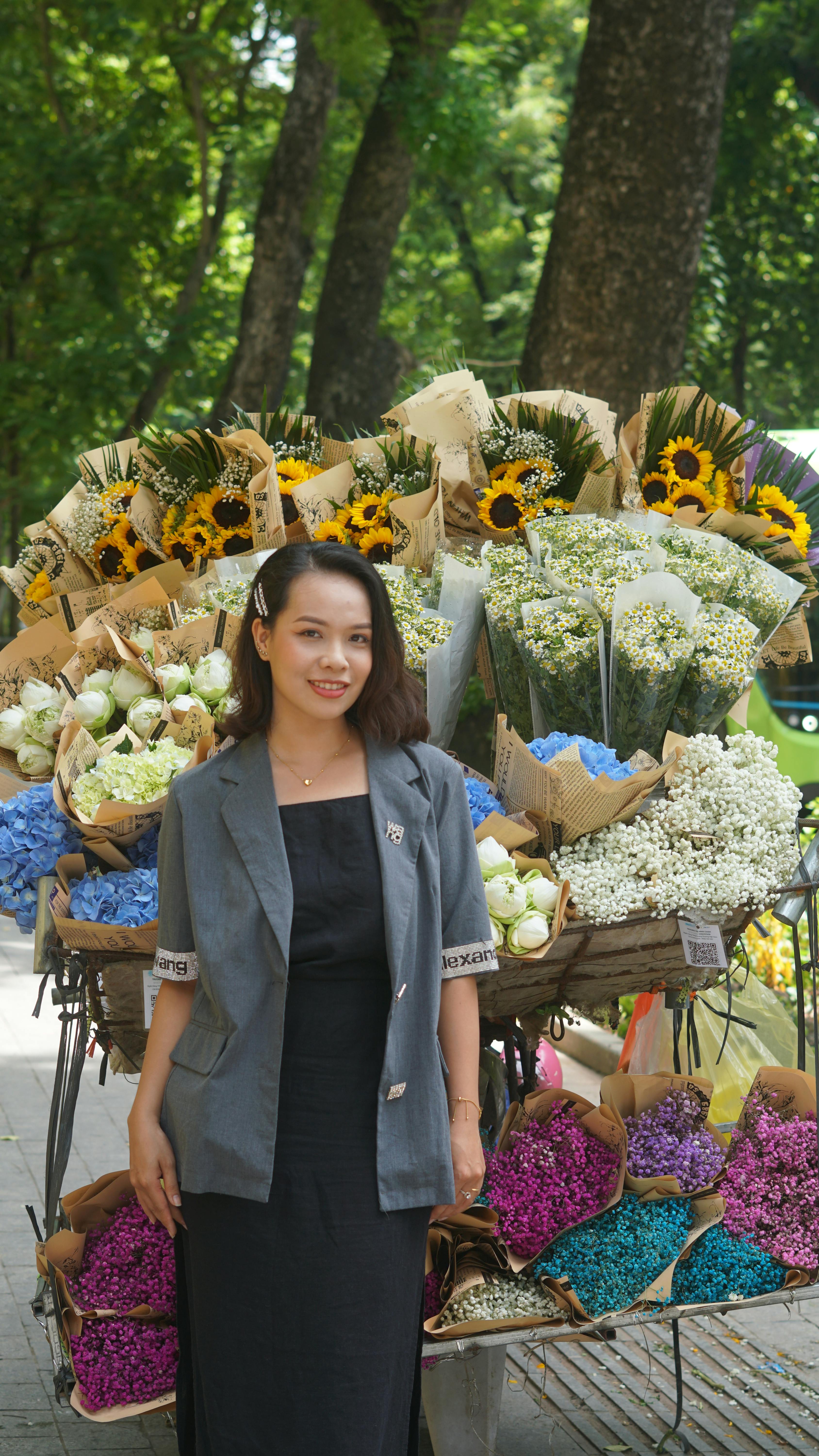 A woman smiles while standing beside an array of vibrant flower bouquets in a lush outdoor setting.
