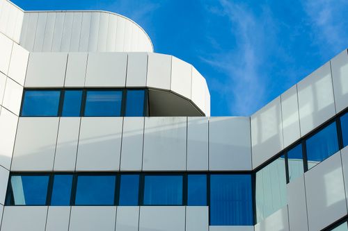 Free Sleek modern building with white panels and glass windows under a clear blue sky. Stock Photo