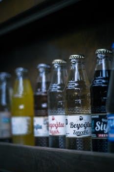 A vertical shot showcasing various beverage bottles with labels arranged on a wooden shelf in dim lighting.