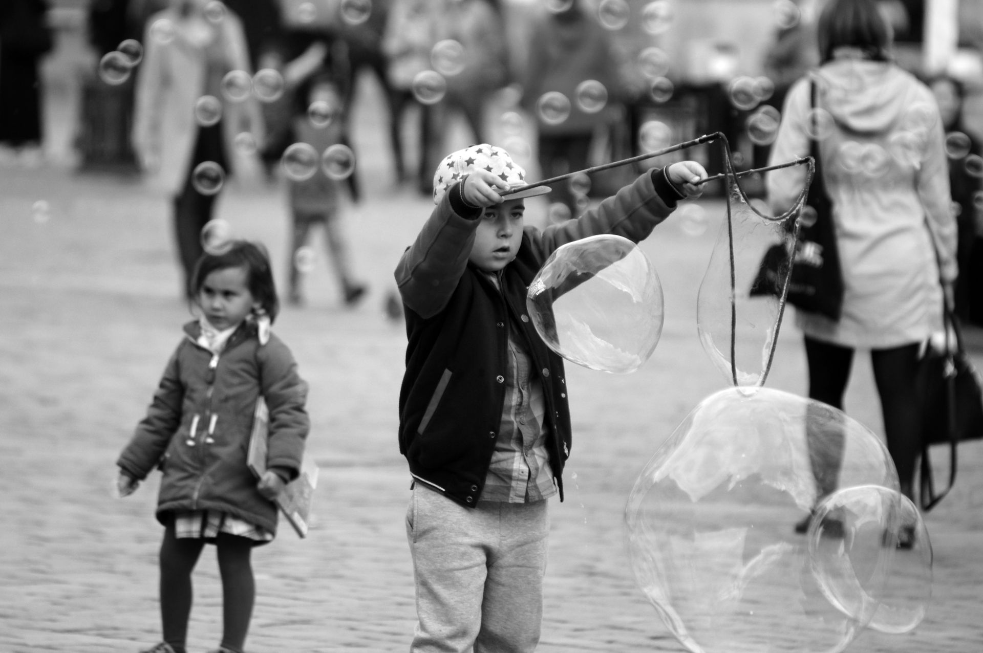 Black and white photo of children making soap bubbles on an urban street, capturing playful moments.