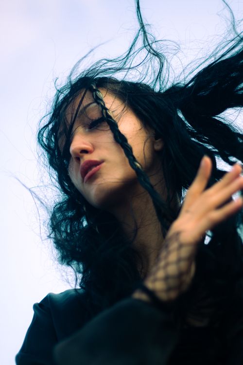 Free A young woman with flowing black hair, eyes closed, and hand raised, captured in a dramatic upward angle. Stock Photo