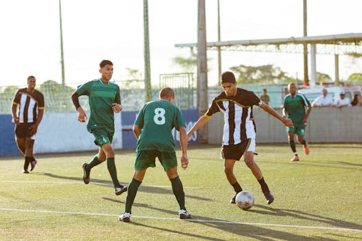 Five male soccer players in action during a daytime soccer match on an outdoor field.