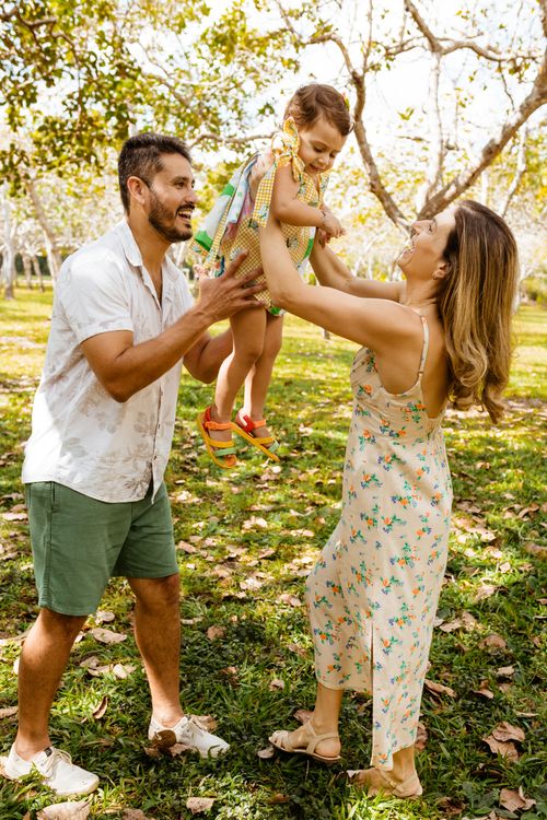 Free A joyful family shares a playful moment outdoors, lifting their daughter in a sunny park. Stock Photo