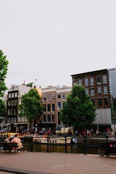 Traditional Amsterdam canal houses with people and trees along the waterfront street.
