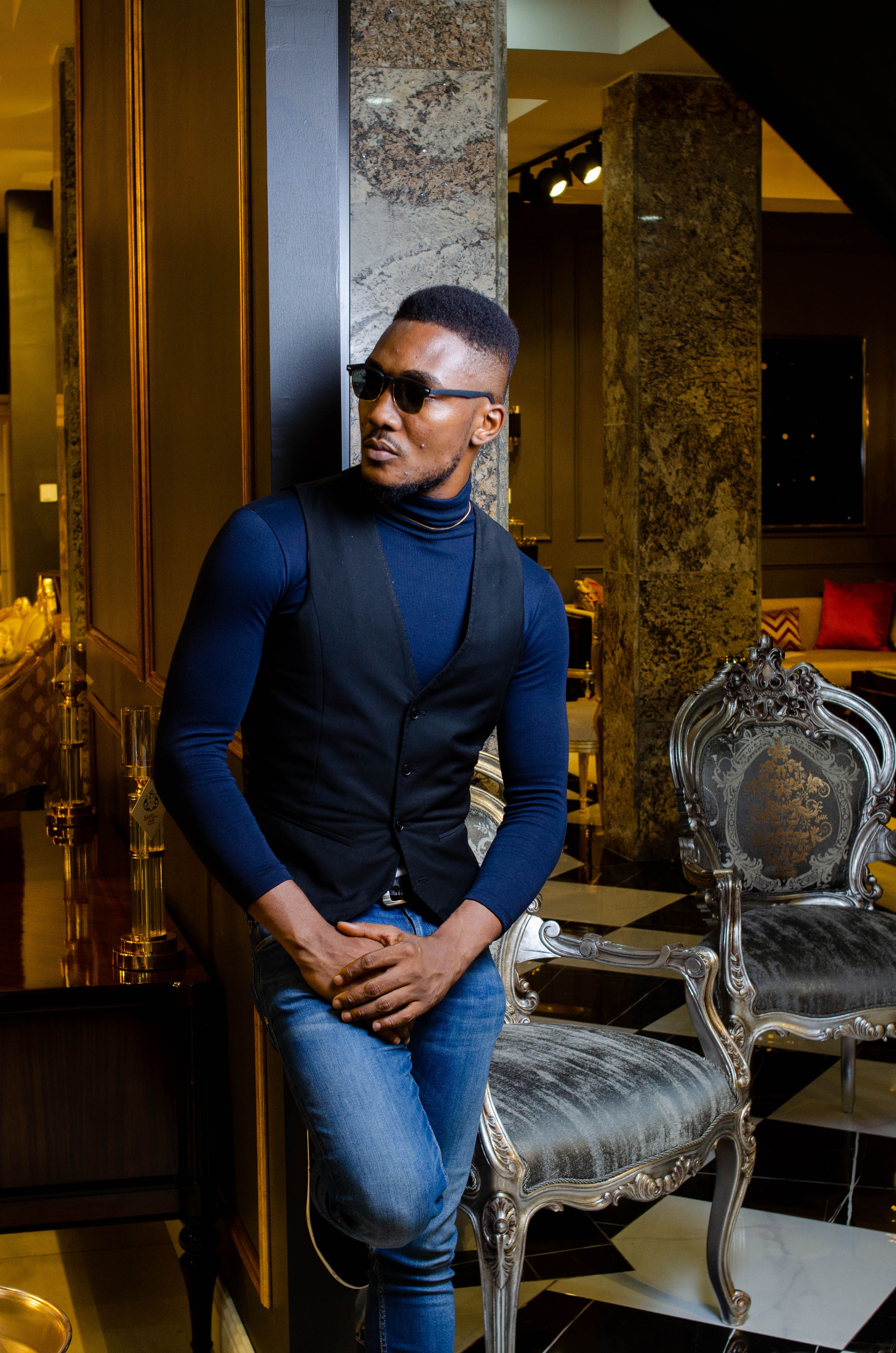 Young man in stylish attire posing indoors with luxury furniture.