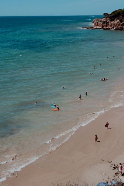 Free A scenic aerial view of a sandy beach with people enjoying the shoreline and turquoise sea. Stock Photo
