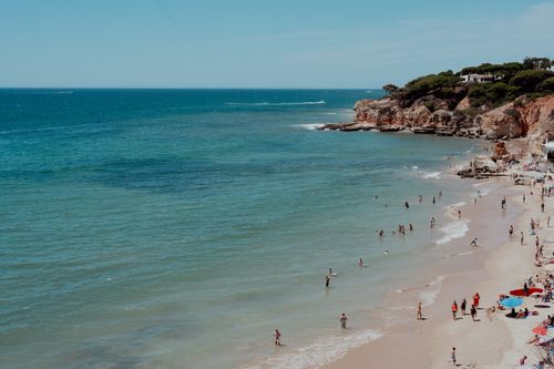 Free A sunny beach scene with people enjoying the ocean and shoreline, ideal for summer vibes. Stock Photo
