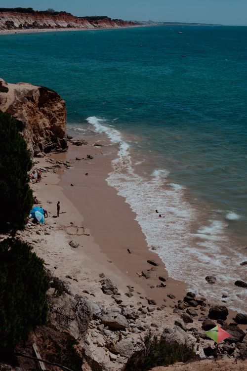 Free Aerial view of a sandy beach with dramatic cliffs and turquoise ocean waters under a sunny sky. Stock Photo