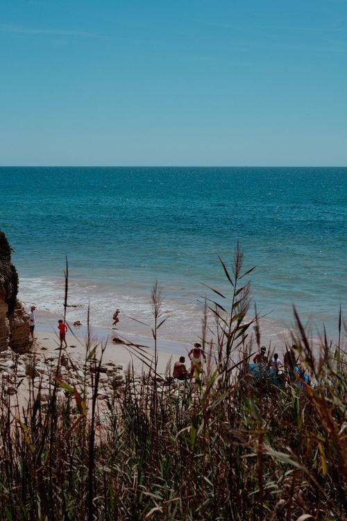 Free Serene beach scene with turquoise waters, rocky cliffs, and people enjoying the summer day. Stock Photo