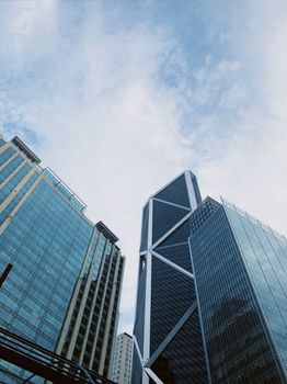 Low-angle shot of glass skyscrapers with modern architecture against a cloudy blue sky.