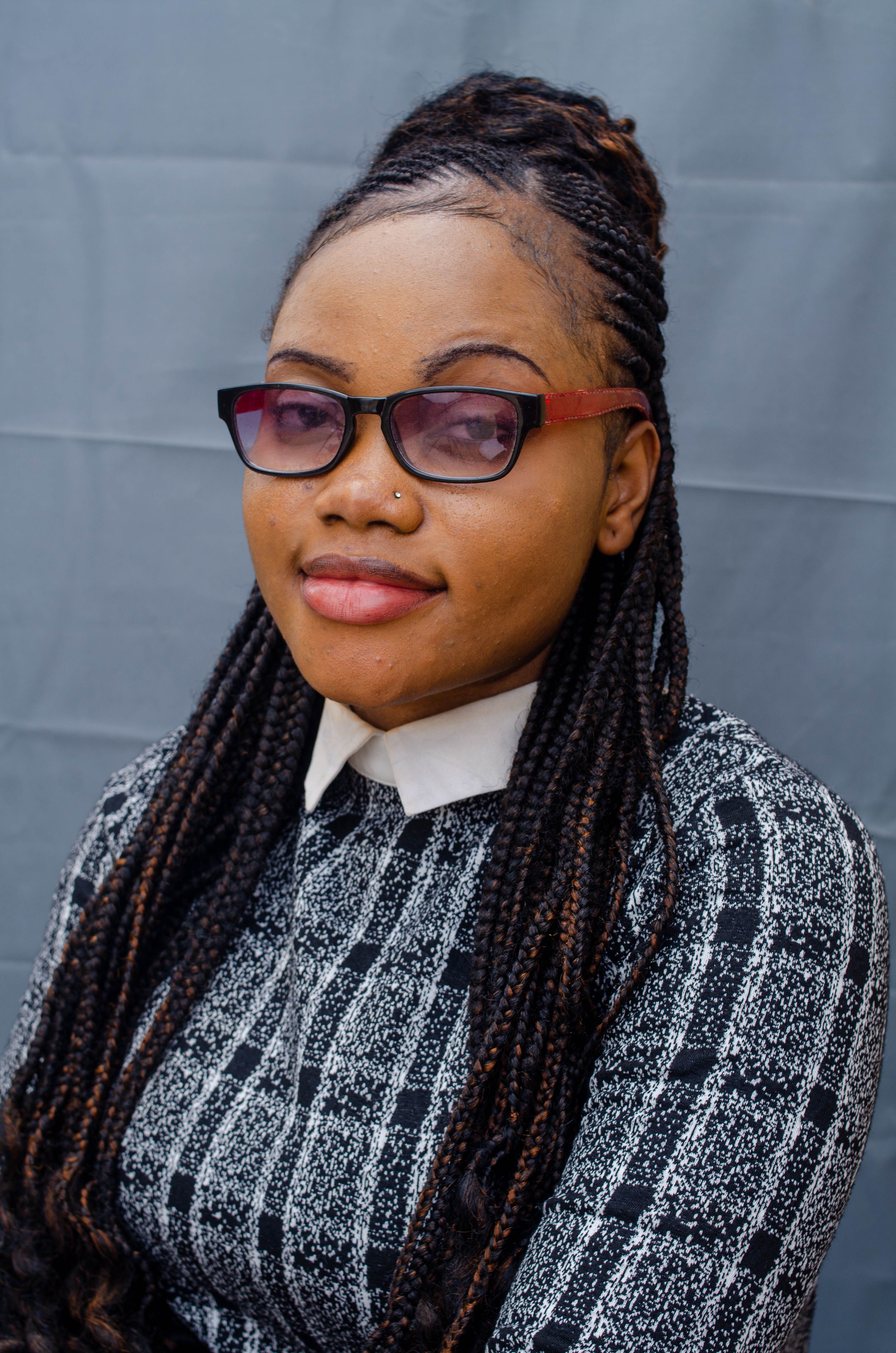 Fashion portrait of a woman with braids and eyeglasses against a gray background.