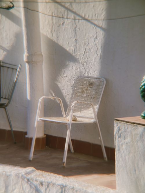 Free White chair on sunlit terrace, evoking rustic charm in Frigiliana. Stock Photo