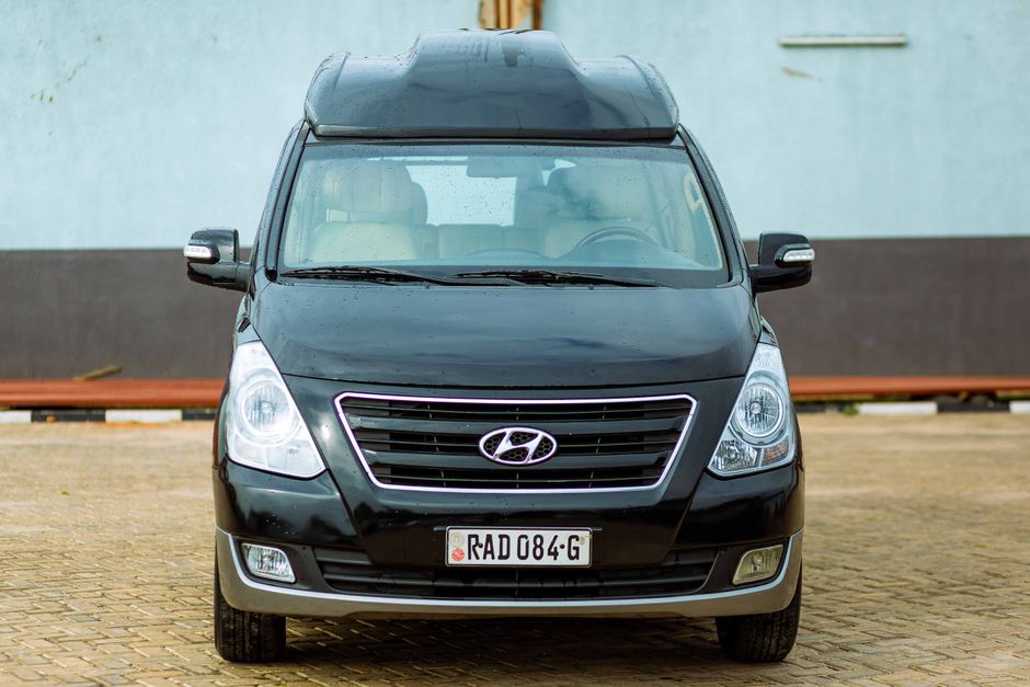 A clean black Hyundai van is parked outdoors on a paved surface, showcasing its front design.