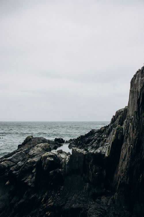 Free A dramatic view of rugged coastal cliffs against an overcast sea, evoking tranquility and isolation. Stock Photo