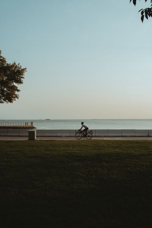Free A lone cyclist rides along a coastal path, enjoying a serene seascape under a clear sky. Stock Photo