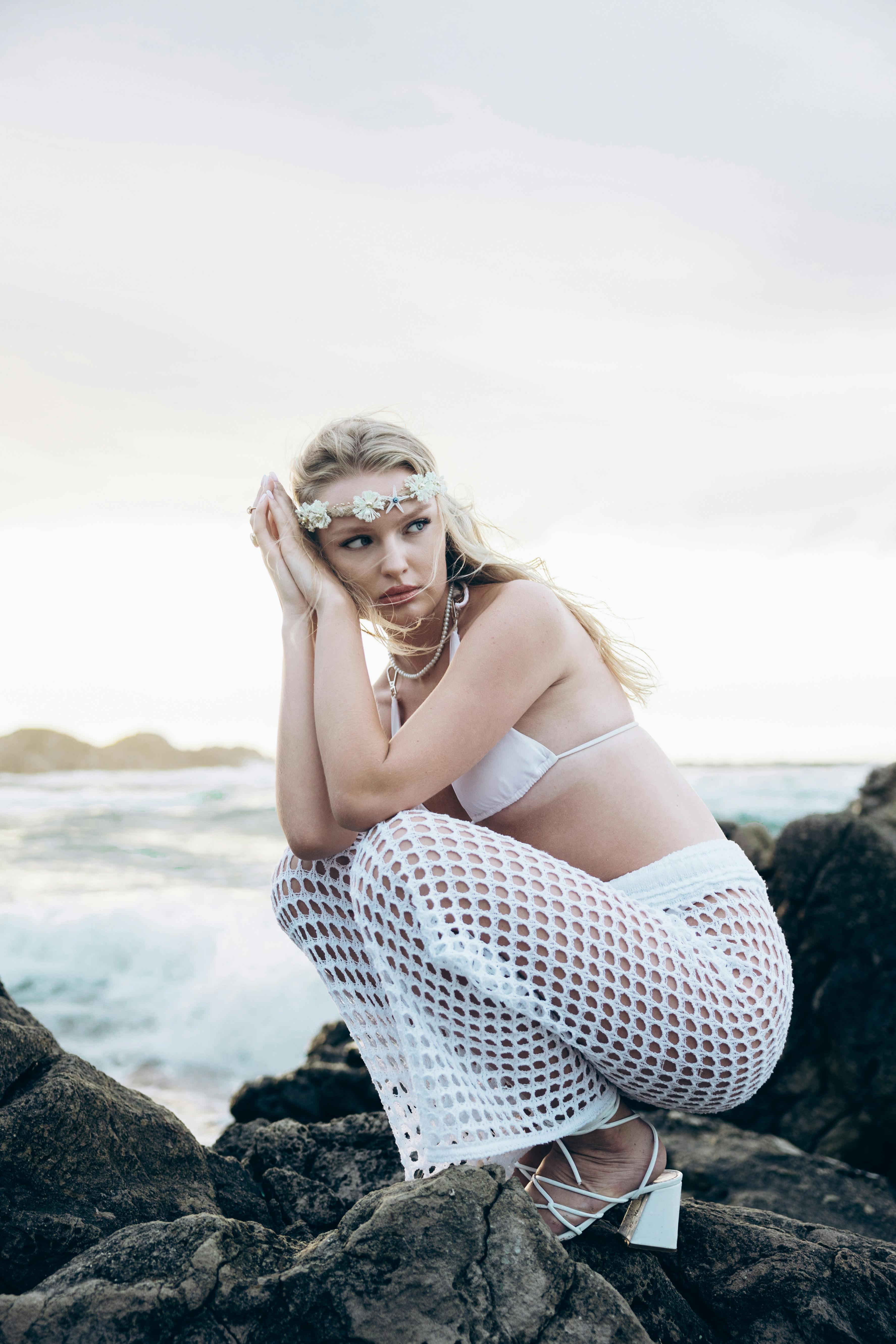 a woman in white bikini sitting on rocks