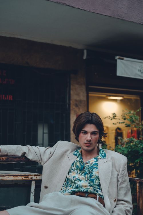 Free A well-dressed young man in a tropical shirt relaxes outdoors, exuding fashion and serenity. Stock Photo