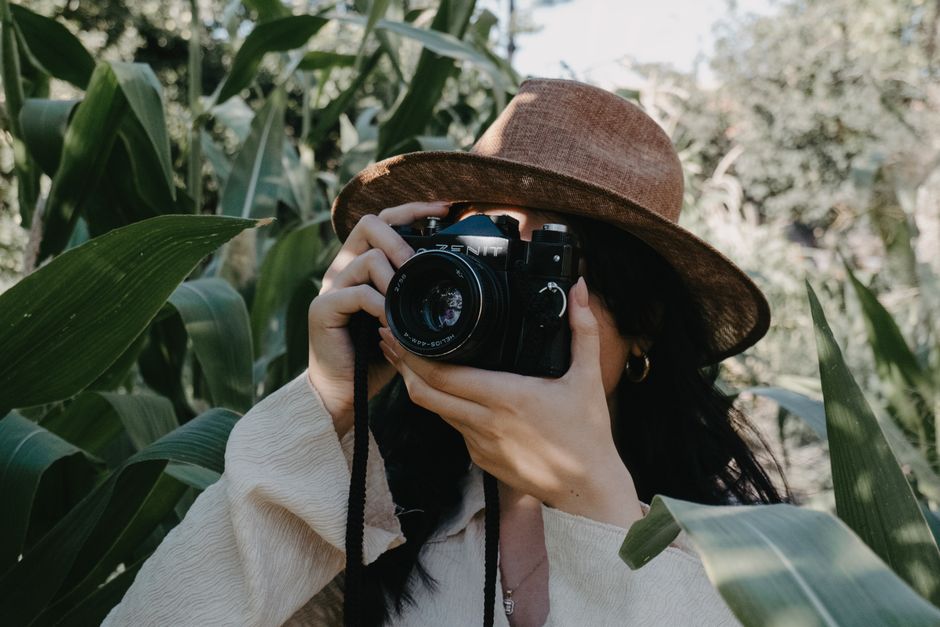 Woman enjoying outdoor photography with a vintage camera in lush greenery.