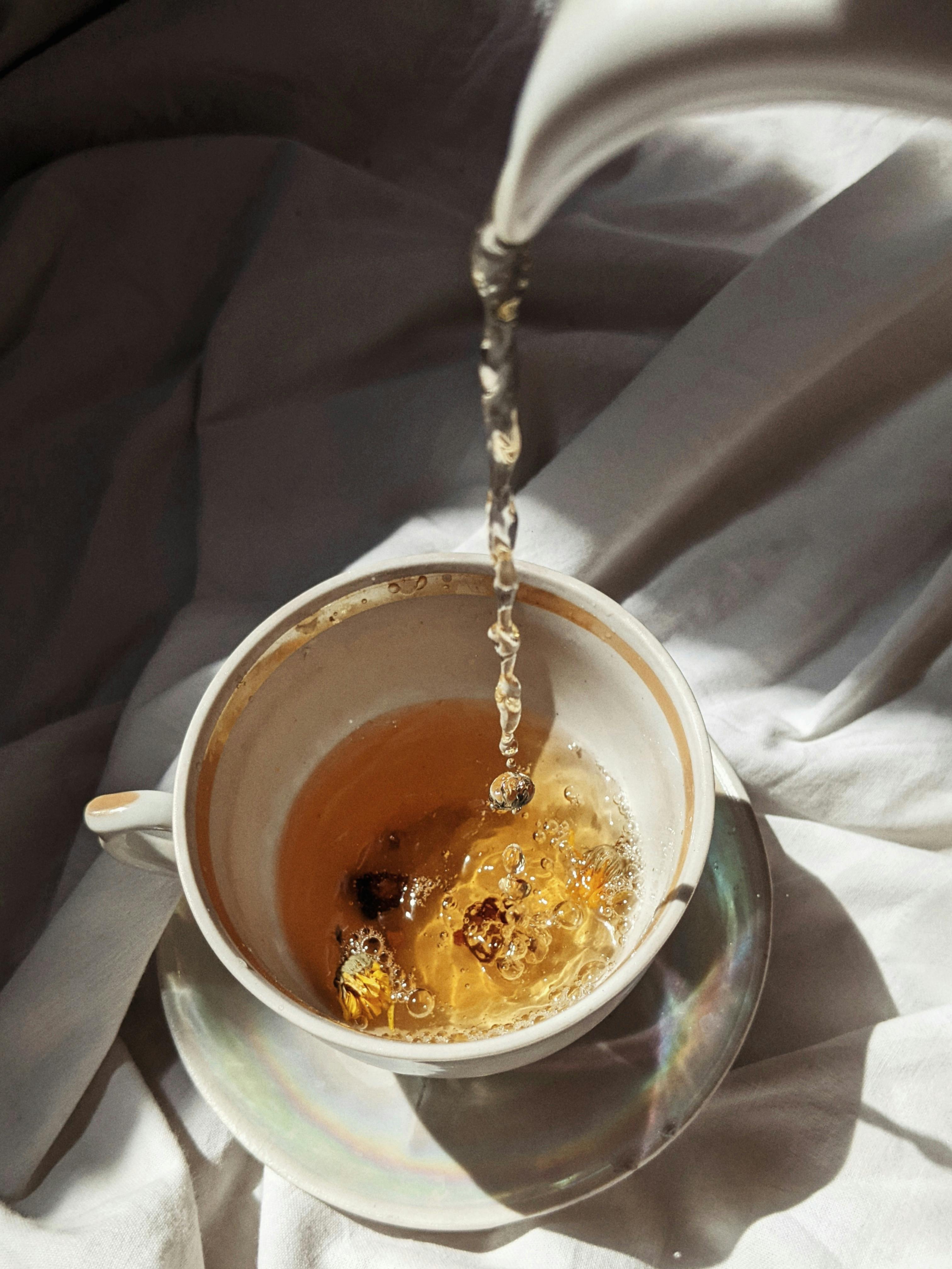 Nick of tea being poured into a ceramic cup on a soft fabric background, capturing tranquility.