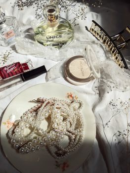 Chic flat lay displaying pearls, perfume, and cosmetics on a draped white fabric.