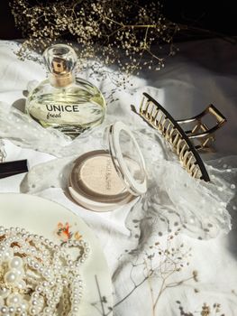 Chic flat lay featuring perfume, makeup, and jewelry on white fabric.