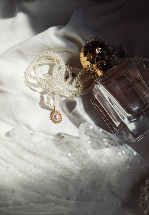 Perfume Bottle and Jewelry on White Fabric