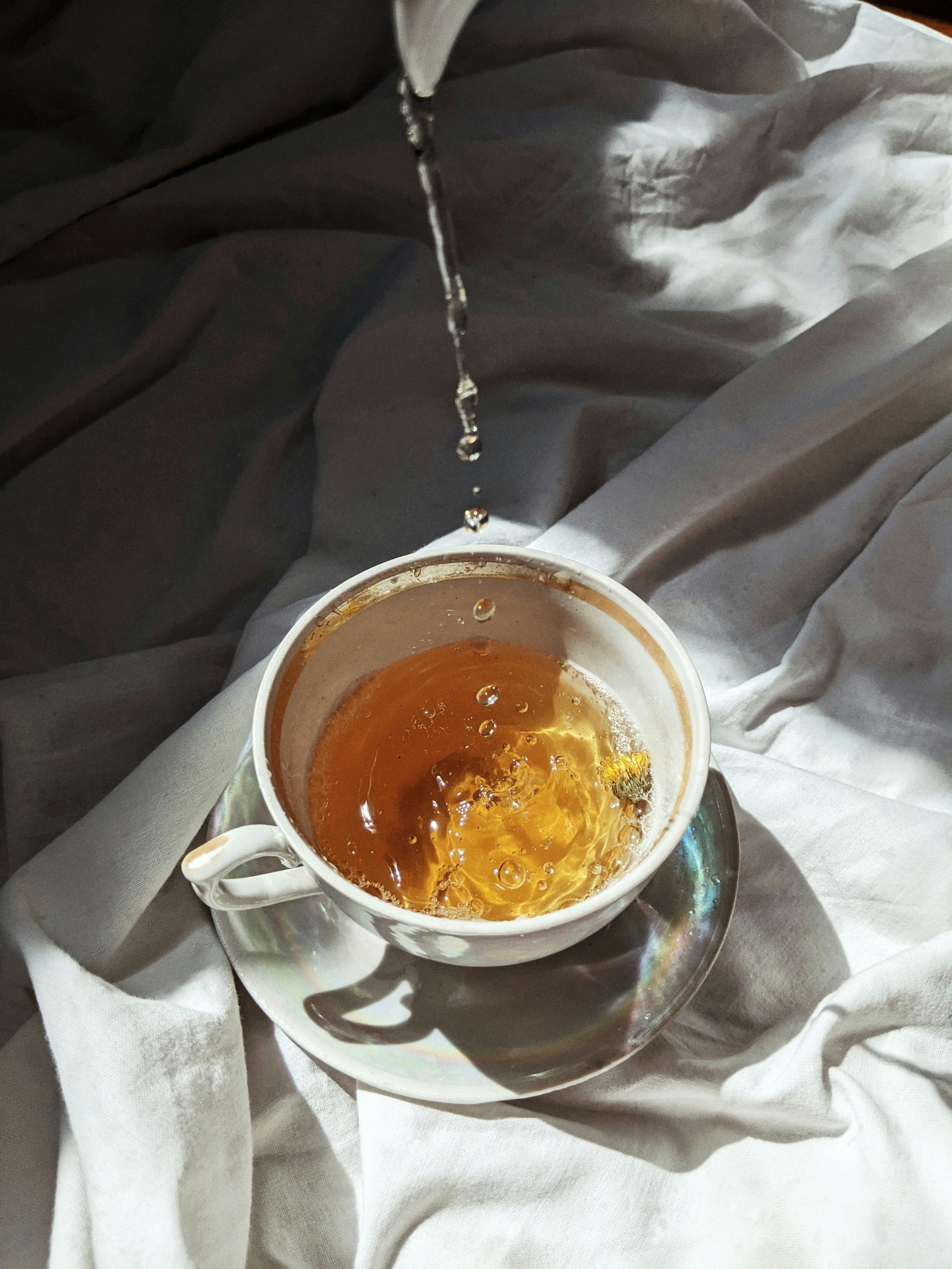 Vertical shot of tea being poured into a ceramic cup over white fabric, highlighting a serene morning aesthetic.