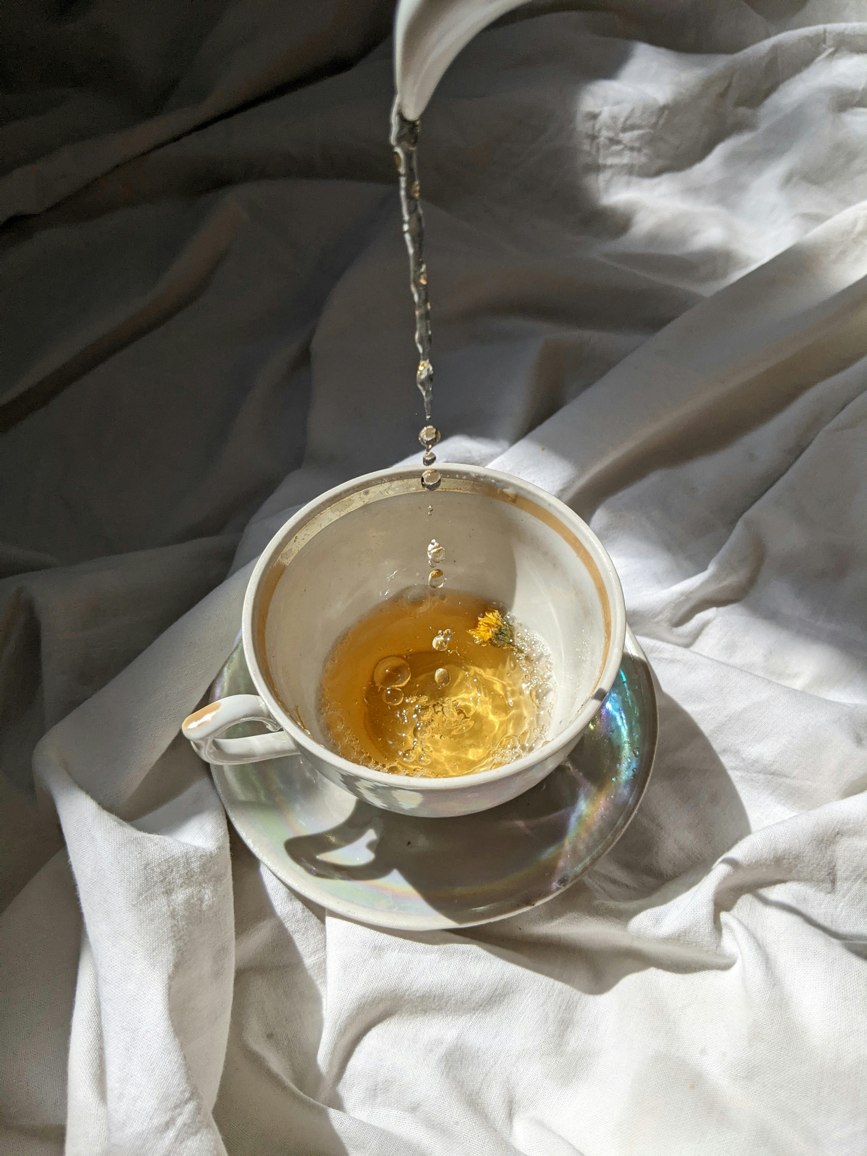 Aesthetic overhead shot of tea being poured into a ceramic cup with soft fabric background, highlighting morning simplicity.