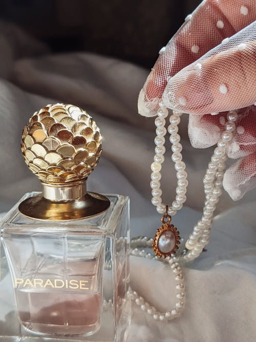 Hand Holding Pearls next to a Perfume Bottle