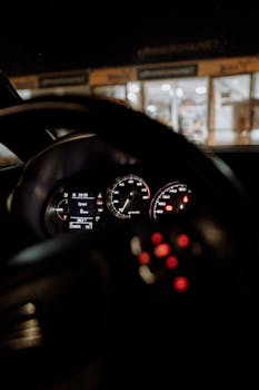 Interior view of a car's illuminated dashboard focusing on the speedometer and steering wheel.