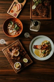 Top view of beautifully arranged gourmet dishes on a wooden table, featuring pasta, meat, and seafood.
