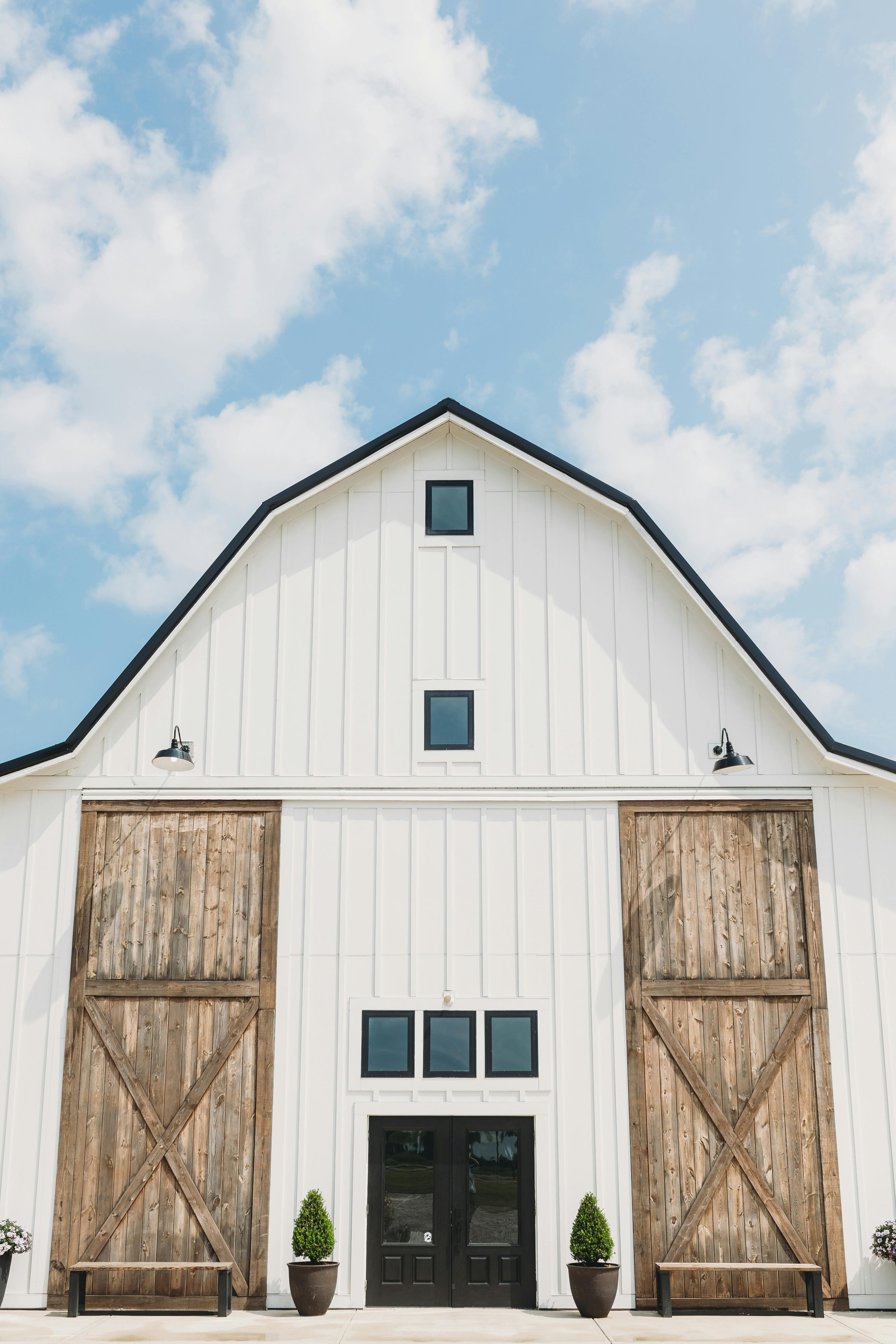 Rustic white barn with wooden doors under a bright blue sky, perfect for rural and farmhouse themes.
