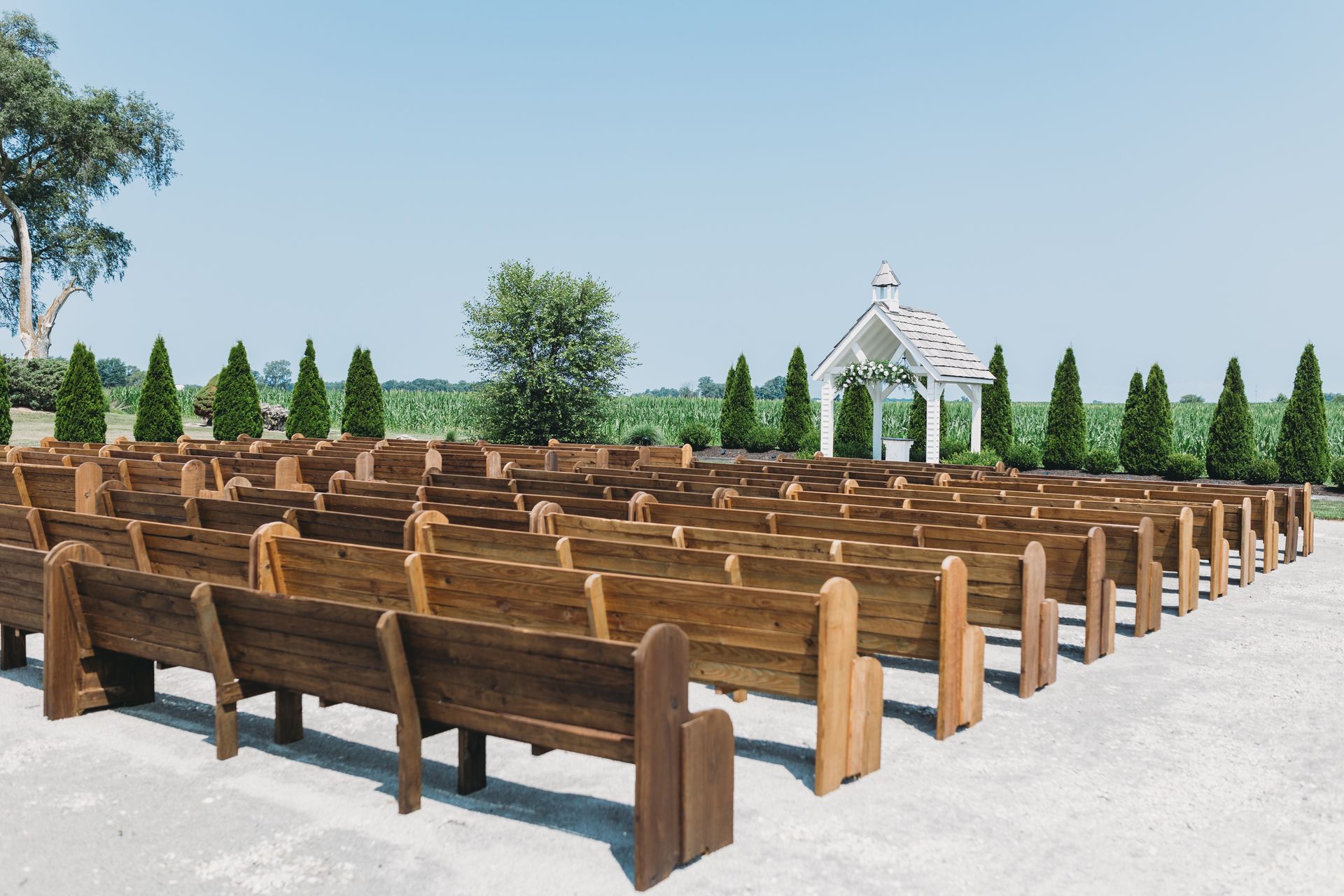 Outdoor wedding venue with rows of wooden benches facing a chapel. Perfect for summer nuptials.