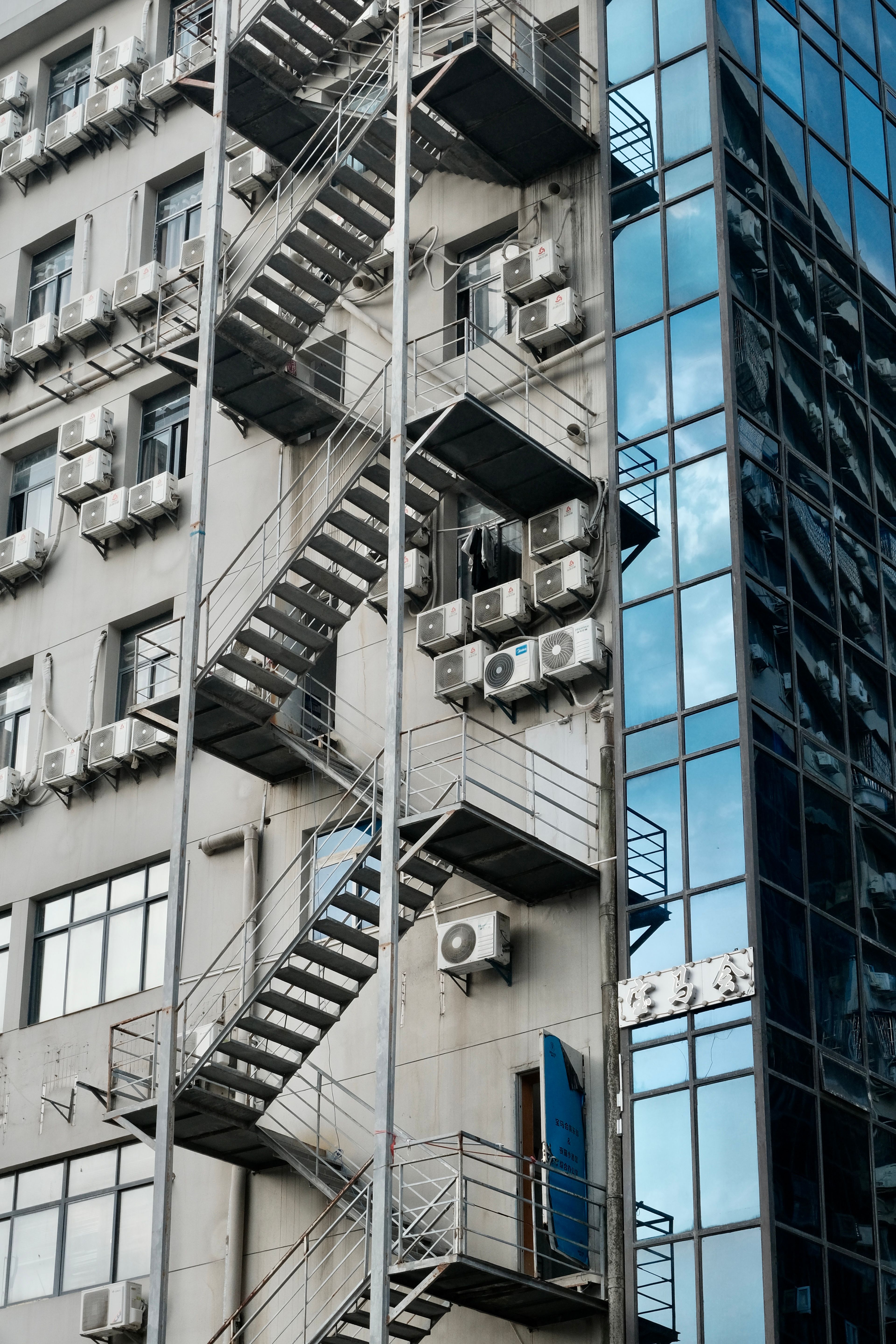 Vertical shot of a modern building with metal fire escape and air conditioners reflecting urban architecture.
