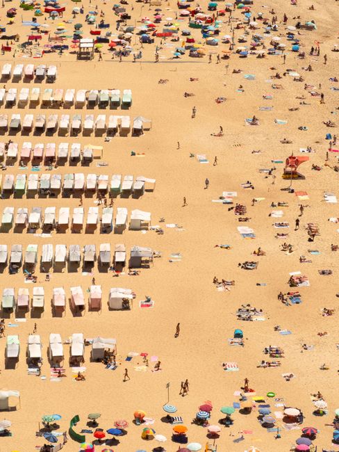 Vibrant aerial shot capturing sunbathers and colorful umbrellas on a sandy beach during summer.