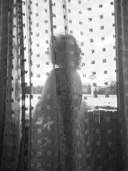 Artistic black and white photo of a woman's silhouette behind a decorative curtain.