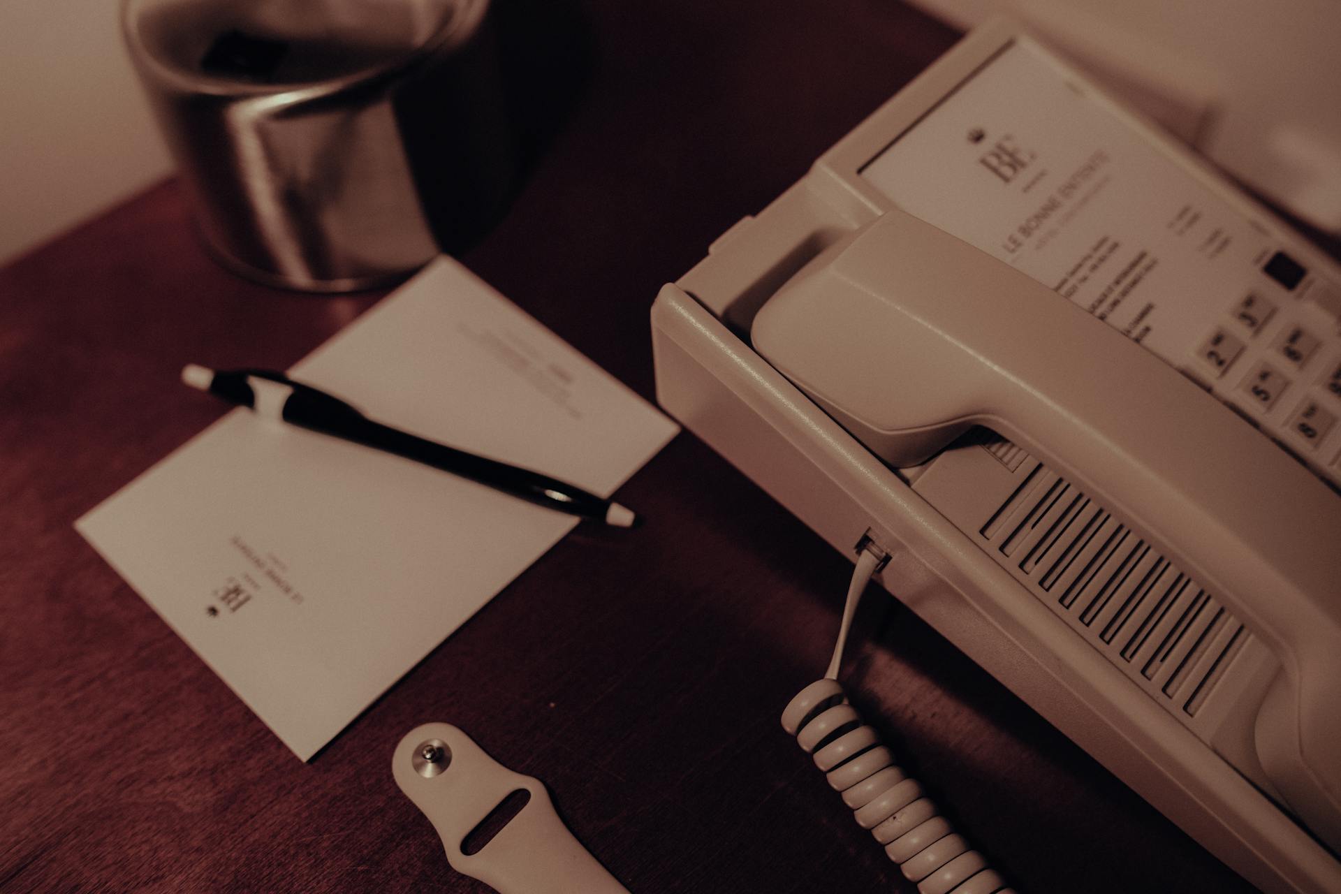 A close-up of a vintage office desk featuring a telephone, notepad, and pen.