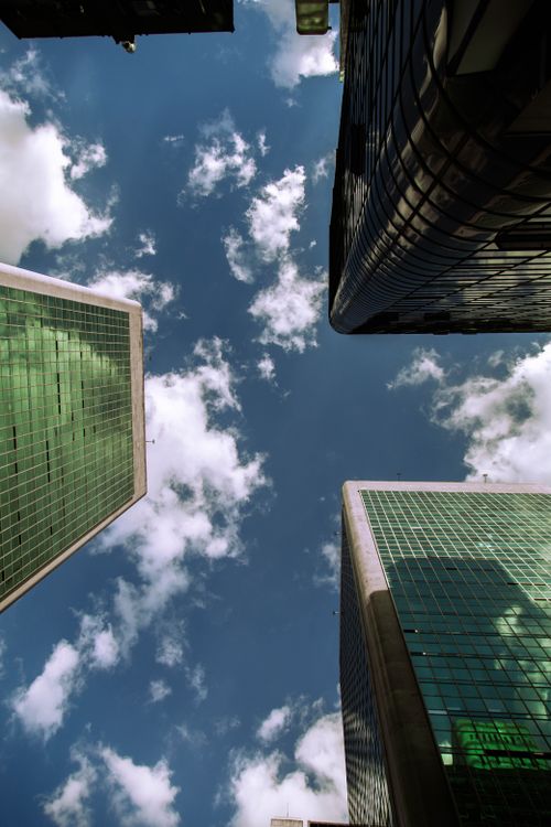 Free A low angle view of modern skyscrapers against a bright blue sky with clouds. Stock Photo