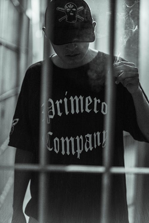 Young Man in Black T-Shirt and Baseball Cap Posing behind Bars