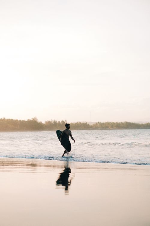 Free A lone surfer with a surfboard running towards the ocean during sunrise, creating a serene silhouette on the beach. Stock Photo