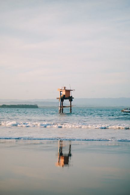 A lone tower stands above calm ocean waters with a distant shoreline.